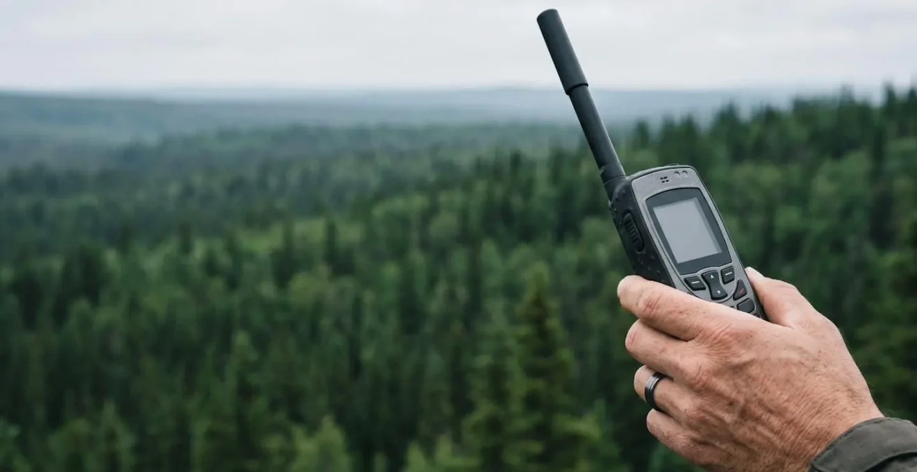 Main tenant un téléphone satellite avec antenne déployée dans un environnement de forêt boréale isolée